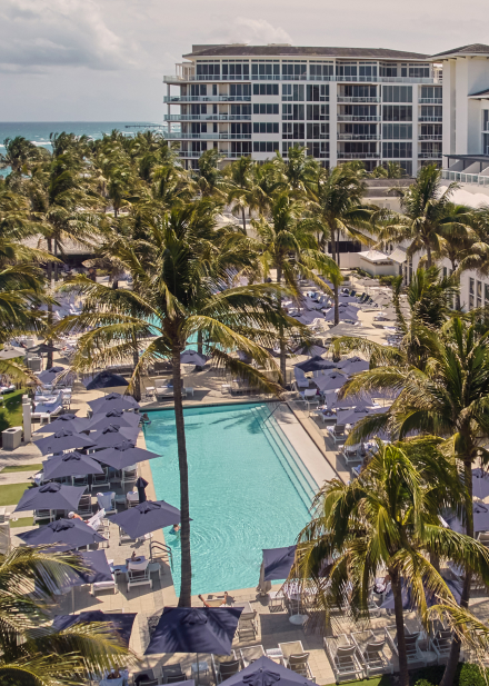 view of the pools of Beach Club surrounded by umbrella, beach chairs and palm trees